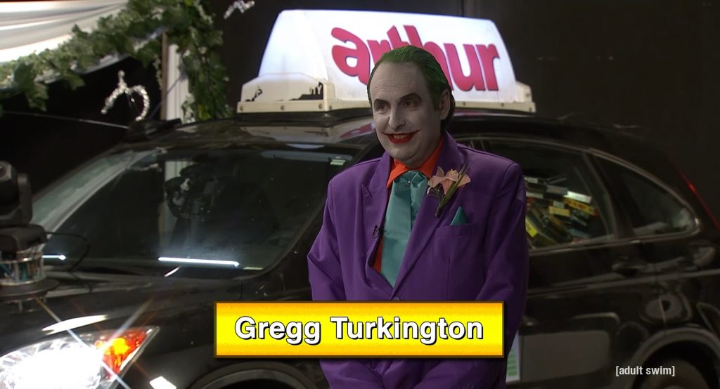 Gregg Turkington in a purple outfit, white facepaint, and green hair as the Joker